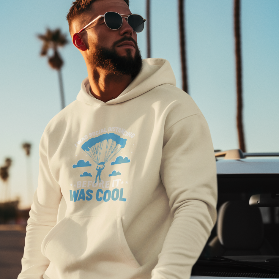 Man wearing sunglasses and sand beige 'I was social distancing before it was cool' hoodie, featuring a parachute design