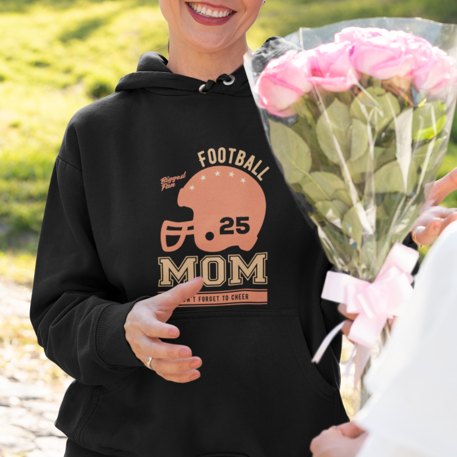 A mom wearing a black hoodie with "Football Mom: Don't Forget to Cheer" text, by holding a bouquet of flowers 