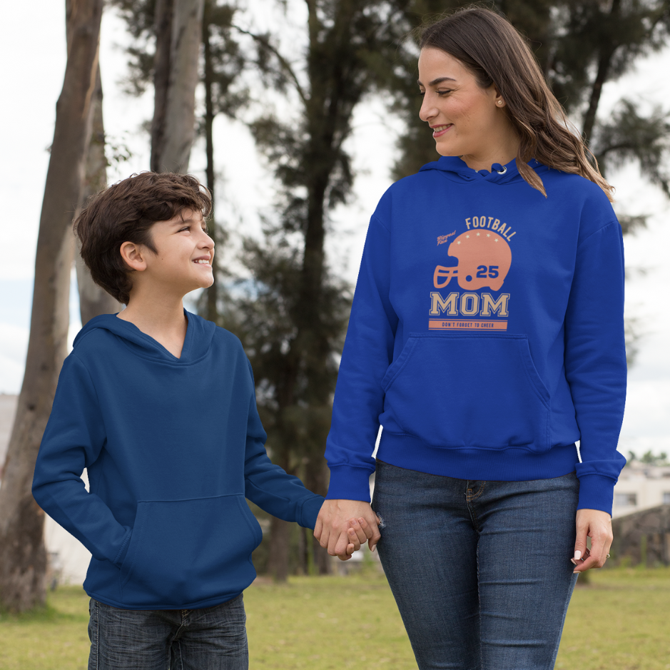 A mom wearing a royal blue hoodie with "Football Mom: Don't Forget to Cheer" text, standing with her son wearing a dark blue  hoodie in a garden.